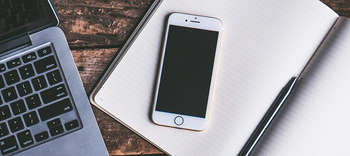 Bachelor Journalismus Ausschnitt eines Notebooks. Rechts daneben liegt ein Schreibblock, darauf ein Handy.