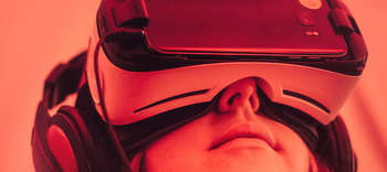 Bachelor Mensch-Computer Interaktion Eine Nahaufnahme von einer Frau, die eine VR-Brille trägt. Das Bild hat einen intensiven roten Unterton.