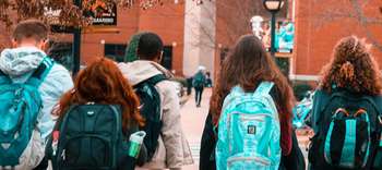 Bachelor Realschullehramt Die Rückenansicht fünf Schüler, die sich auf den Weg zur Schule machen. Sie tragen verschiedenfarbige Schulrucksäcke.