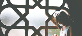 Judaistik Auf dem Bild befindet sich ein großes rundes Fenster aus Milchglas. Auf diesem ist ein Fenster-Ornament aus dunklem Holz angebracht. In dem Muster ist der Davidstern erkennbar. Vor dem Fenster ist ein Mann mit etwas längeren Haaren zu sehen. Dieser nimmt nur einen kleinen Teil des Fensters ein, wodurch das Außmaß des Fensters deutlich wird.