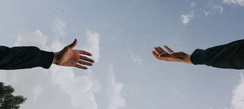 Bachelor Therapie Ausschnitt der Arme zweier Personen, die versuchen sich zu berühren. Das Bild ist von unten fotografiert, sodass der Himmel zu sehen ist.