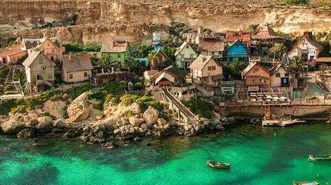 Aufnahme eines Ausschnitts Maltas aus der Luft. Zu sehen ist ein Dorf direkt am Meer umgeben von türkisblauem Wasser.