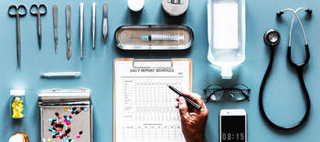 Bachelor Gesundheitsmanagement Tisch, auf dem verschiedene medizinische Instrumente platziert sind. Unter diesen ein Stethoskop, eine Brille, ein Klemmbrett sowie verschiedene Medikamente.