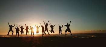 Bachelor Soziologie Ein Strand im Sonnenuntergang. Elf Personen springen dabei hoch in die Luft und strecken die Arme aus.