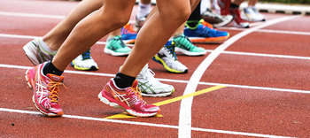 Bachelor Sport Nahaufnahme einer Laufbahn, auf der sich mehrere Läufer für ein Rennen bereit machen. Zu sehen sind die Beine der Personen mit Fokus auf derer Sportschuhe.