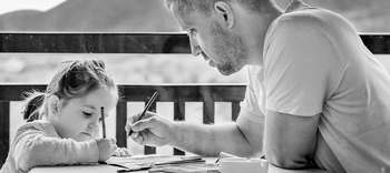 Pädagogik & Lehre Auf der Schwarz-Weiß-Aufnahme sieht man einen Vater mit seiner kleinen Tochter. Sie zeichnen gemeinsam ein Bild.
