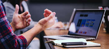 Bachelor Personalmanagement Ausschnitt eines Meetings. Zwei Personen sitzen an einem Schreibtisch vor einem aufgeklappten Laptop. Eine der Personen gestikuliert stark.