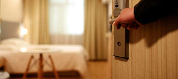 Bachelor Hotelmanagement Eine Person öffnet die Tür eines Hotelzimmers. Im Fokus ist die Hand, welche die Tür öffnet. Das Zimmer ist modern und in freundlichen Farbtönen eingerichtet.