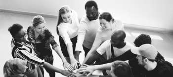 Sozial- und Verhaltenswissenschaften Auf der Schwarz-Weiß-Aufnahme ist eine Gruppe junger Studenten unterschiedlicher Herkunft abgebildet. Sie stehen in einem Kreis und ihre Hände berühren sich als Zeichen der Verbundenheit.