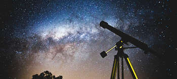 Bachelor Astronomie Fotografiert wurde ein Teleskop von unten. Über dem Teleskop ist der tiefblaue Nachthimmel mit unzähligen Sternen erkennbar.