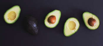 Bachelor Lebensmitteltechnologie Das Bild zeigt fünf halbe Avocados auf einem dunklen Hintergrund. Diese sind nebeneinander angeordnet. Vier davon zeigen das gelb-grüne Innere der Avocados, während eine Hälfte die Rückseite zeigt.