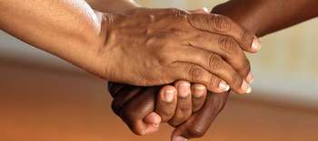 Psychologie Nahaufnahme der Hände zweier Personene. Die eine Person umfasst mit ihren Händen die Hand der anderen Person.