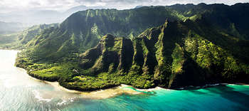 Bachelor Geographie Luftaufnahme einer malerischen grün bewachsenen und hügeligen Insel. Umgeben ist die Insel von türkisblauem Meer. Über Meer und Insel legen sich Sonnenstrahlen.