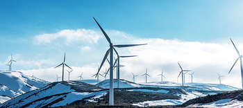 Bachelor Energiemanagement Fotografie einer Bergkulisse mit Windrädern. Einige von ihnen sind in der Ferne erkennbar. Die Berge sind zu großem Teil mit Schnee bedeckt.