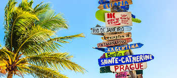 Bachelor Tourismus Auf der linken Seite des Bildes eine Palme. Rechts daneben ein bunter Wegweiser, der Urlaubsorte wie Rio de Janeiro, Argentinien oder Prag anzeigt.