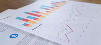 Bachelor Wirtschaftswissenschaften Nahaufnahme zweier Zettel mit Grafiken und Diagrammen. Auf dem Zettel die Beschriftung BUSINESS ITEMS.