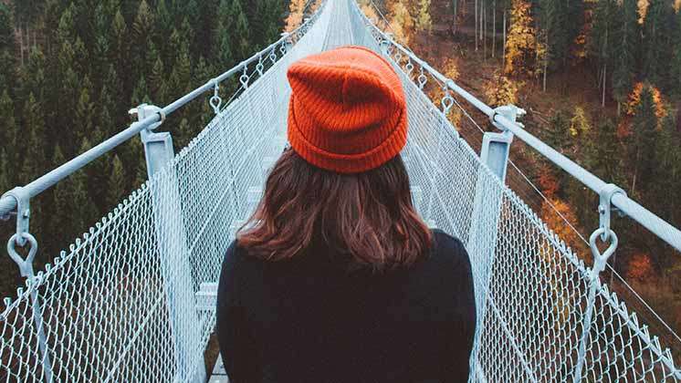 Der örtliche NC, auch Orts-NC Ein Mädchen mit einer orangenen Pudelmütze steht mit dem Rücken zum Betrachter am Rand einer Hängebrücke. Es ist Herbst.
