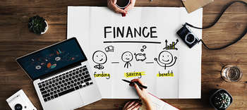 Bachelor Finance Ausschnitt eines Schreibtisches, an dem sich zwei Personen gegenüber sitzen. Auf dem Tisch ein Laptop sowie ein Plakat mit der Aufschrift FINANCE.