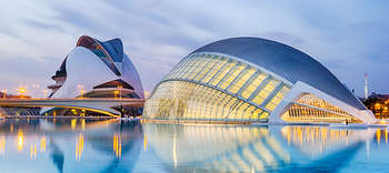 Bachelor Architektur Zwei weiße kuppelfärmige Gebäude im Abend, welche sich direkt am Wasser befinden. Die rechte Kuppel hat eine detailreiche Glasfront, aus der sanftes Licht scheint. Dazu spiegeln Straßenlaternen ihr Licht im Wasser.