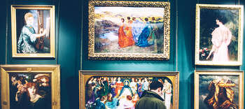 Kunstgeschichte Erkennbar ist ein Ausschnitt einer petrolfarbenen Museumswand. An der Wand hängen in goldenen Bilderrahmen antike Zeichnungen und Kunstwerke. Vor den Bildern steht ein Mann in einer grünen Jacke.