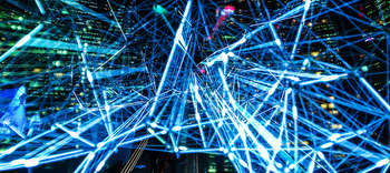 Bachelor Technologiemanagement Im Hintergrund lässt sich eine Großstadt bei Nacht erahnen. Im Fokus zahlreiche leuchtende Lichtstrahlen in bunten Farben.