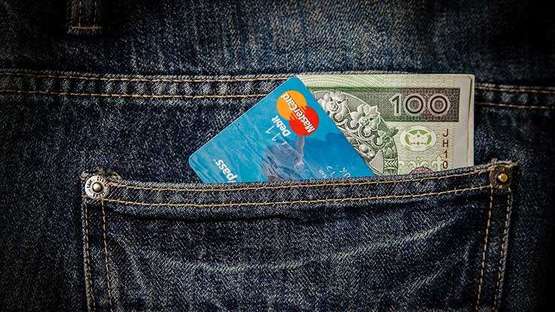 Nahaufnahme einer Hosentasche, in der sich einer Kreditkarte und ein Geldschein befinden. 