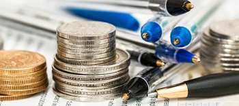 Bachelor Steuerrecht Nahaufnahe von Münz-Stapeln auf einem Formular. Naneben mehrere blaue und schwarze Kugelschreiber.