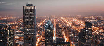 Bachelor Urbanistik Eine Großstadt in der Abenddämemrung. Im Vordergrund stehen Wolkenkratzer und andere Hochhäuser, der Hintergrund zeigt die weite der Stadt. Es sind unzähliche orangfarbene Lichter in der gesamten Stadt erkennbar.