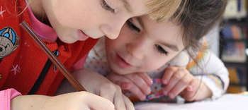 Bachelor Erziehungswissenschaften Nahaufnahme der Köpfe zwei kleiner Mädchen, die zusammen an einem Bild malen.