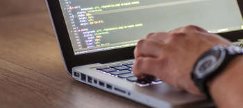 Bachelor Software Engineering Eine Nahaufnahme von den Händen eines Mannes, der an einem Laptop arbeitet. Der Bildschirm des Laptops zeigt HTML-Codes.