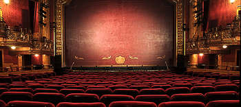 Theater Fotografiert wurde ein pomböser leerer Theatersaal von der Zuschauerperspektive aus. Die Sitze sind in einem edlen rot gehalten und die Theater-Balkone mit goldenen Verzierungen geschmückt.