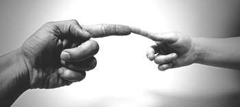 Ethnologie Das Bild zeigt zwei Hände, deren Zeigefinger sich berühren. Die linke Hand gehört einer erwachsenen Person, die rechte Hand einem Kind. Die linke Hand wirkt dunkler, die rechte heller. Gehalten ist das Bild in graustufen.