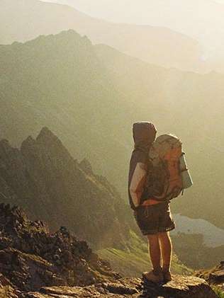 Eine Person steht in einer bergigen Landschaft, durch die einige Sonnenstrahlen fallen. Sie trägt einen Rucksack.