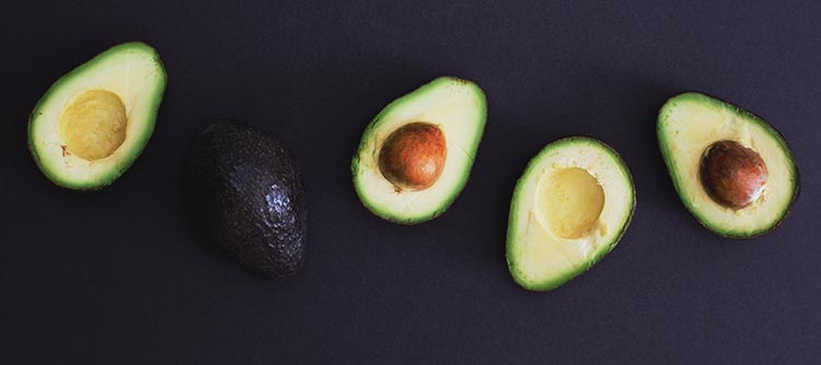 Bachelor Lebensmitteltechnologie Das Bild zeigt fünf halbe Avocados auf einem dunklen Hintergrund. Diese sind nebeneinander angeordnet. Vier davon zeigen das gelb-grüne Innere der Avocados, während eine Hälfte die Rückseite zeigt.