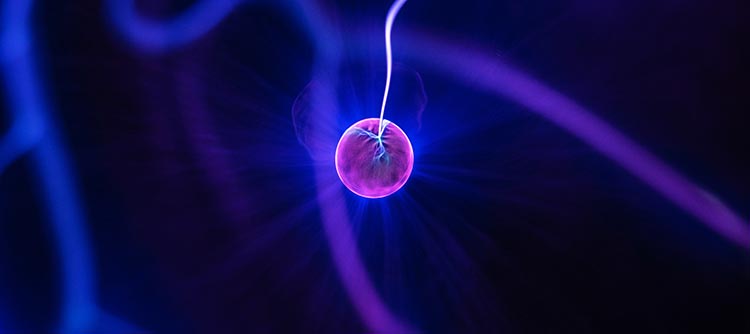Bachelor Nanotechnologie Das Bild zeigt einen Nano-Partikel, der vergrößert dargestellt wurde. Es handelt sich um eine rötlich-violette Kugel im Zentrum des Bildes, welche an einem Strang hängt. Die Partikel leuchten und auch im Hintergrund befinden sich unsschärfe Stränge, die in blau-violettes Licht getaucht sind.