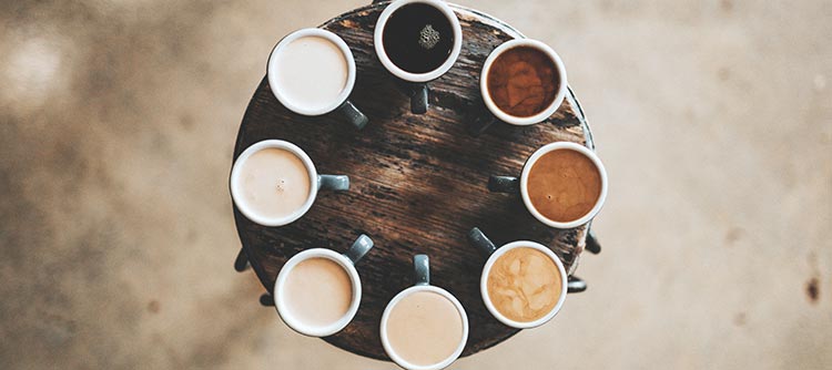 Kulturwissenschaften Erkennbar ist ein rundes hölzernes Tablett, welches aus der Vogelperspektive fotografiert wurde. Auf diesem Tablett sind acht Kaffeetassen wie eine Uhr angeordnet. Der Kaffe auf zwölf uhr ist schwarz. Von diesem Punkt werden die anderen Tassen im Uhrzeigersinn immer heller, sodass eine Farbpalette an Kaffeefarben entsteht.