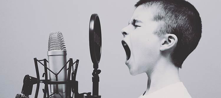 Gesang Das Bild zeigt Kopf und Hals eines Jungen, welcher in ein Studio-Mikrofon sing. Er hat die Augen zum Singen geschlossen und den Mund weit aufgerissen. Das Bild ist in graustufen gehalten.
