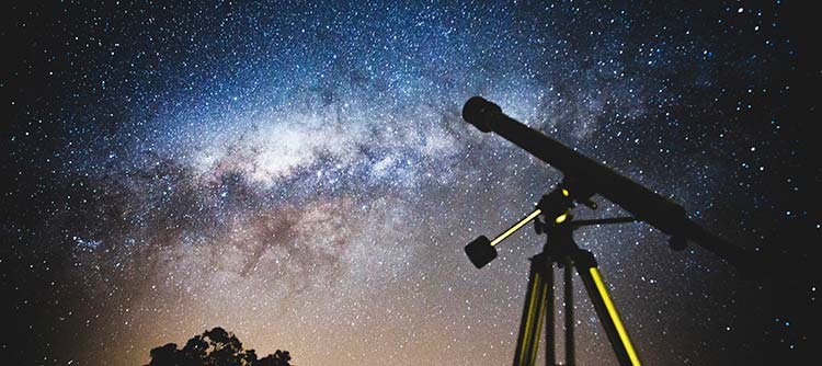 Bachelor Astronomie Fotografiert wurde ein Teleskop von unten. Über dem Teleskop ist der tiefblaue Nachthimmel mit unzähligen Sternen erkennbar.