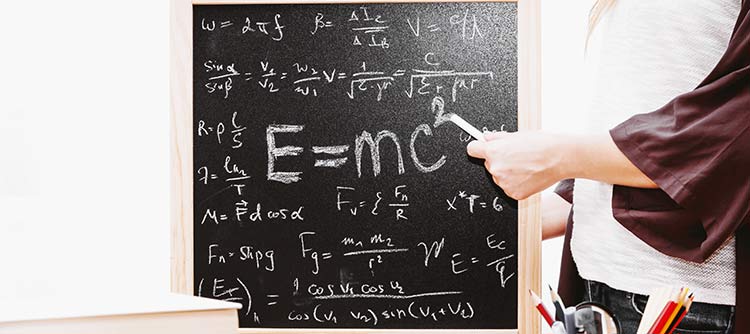 Bachelor Mathematik Eine Tafel mit verschiedenen mathematischen Formeln. In der Mitte steht groß die berühmte Ableitung Einsteins zur Relativitätstheorie. Die Formeln sind alle mit Kreide gezeichnet worden. Rechts neben der Tafel ist eine Person zu erahnen. Diese hält ein Kreidestück und deutet damit auf die Formeln.