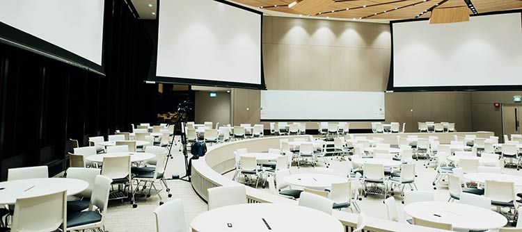 Bachelor Eventmanagement Fotografie eines Veranstaltungssaales mit vielen hellen Runddtischen samt Bestuhlung.