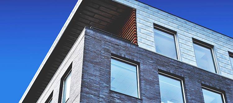 Bachelor Immobilienwirtschaft Ausschnitt eines modern wirkenden Gebäudes von unten fotografiert. Im Hintergrund der klare blaue Himmel.